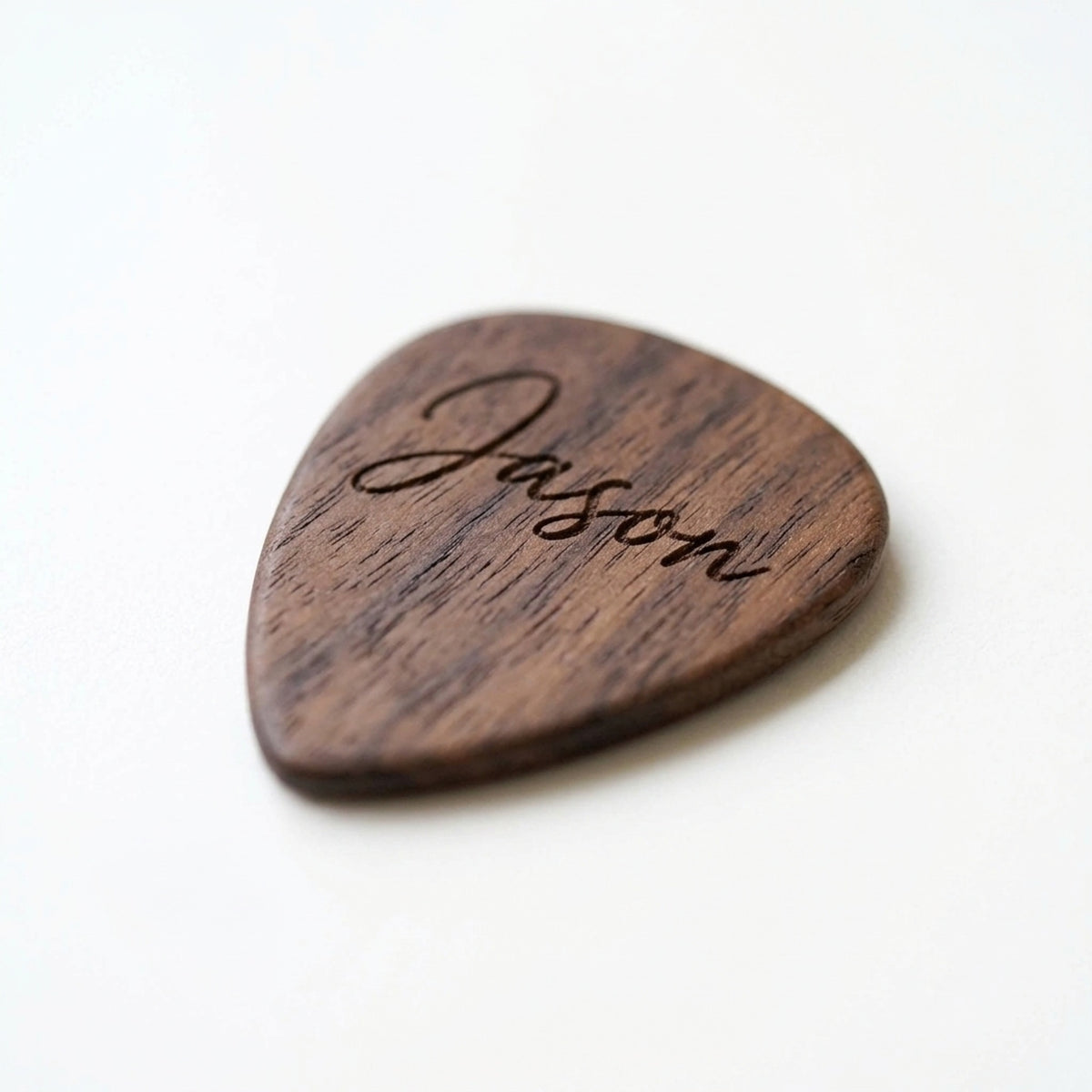 Close-up of a walnut guitar pick engraved with a name in script
